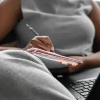 A woman taking notes while researching on a laptop