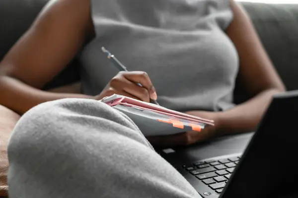 A woman taking notes while researching on a laptop