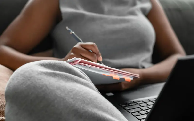 A woman taking notes while researching on a laptop