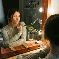 A woman reflecting thoughtfully in a warmly lit mirror