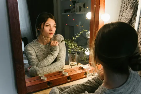 A woman reflecting thoughtfully in a warmly lit mirror